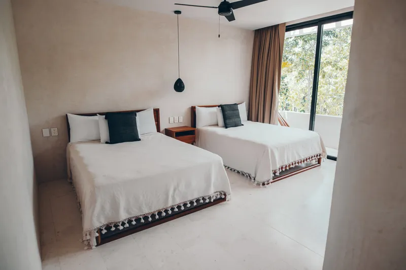 Casa Thomas guest bedroom with two beds, dark gray pillows and a sliding door open to a terrace